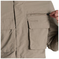 A light tan jacket features a zippered pocket being unzipped by a hand with another patch pocket visible beside it in a neutral setting.