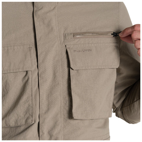 A light tan jacket features a zippered pocket being unzipped by a hand with another patch pocket visible beside it in a neutral setting.