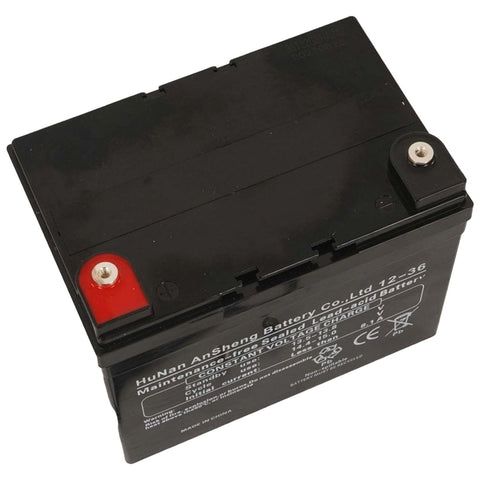 A rectangular black lead-acid battery with red and silver terminals sits on a flat surface displaying technical specifications and labels indicating its capacity and usage.