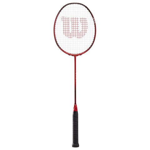 A red badminton racket stands upright with a black handle and a grid string pattern featuring a prominent white "W" logo on the head, ready for play in a sports environment.