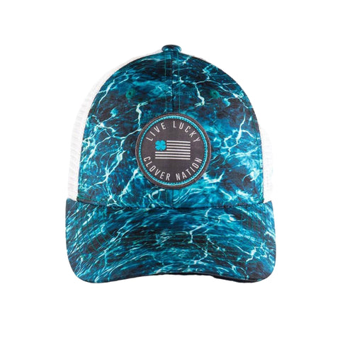 A cap with a blue water-like pattern is positioned upright displaying a circular logo that reads LIVE LUCKY CLOVER NATION against a plain background emphasizing its design.