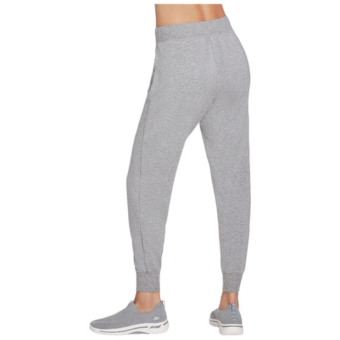 Gray jogger pants are being worn by a person standing in athletic shoes, showcasing a casual outfit suited for exercise or leisure in a relaxed indoor setting.