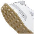 A white athletic shoe with a textured sole featuring small rubber spikes is positioned at an angle showcasing its bottom surface against a plain background, emphasizing its grip and design.