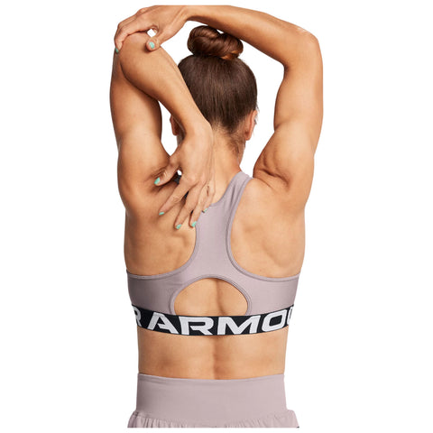 A person stretches their arms behind their head while wearing a light purple sports bra with a black band that reads "ARMOUR" in white letters, showcasing a fit physique and teal nail polish.