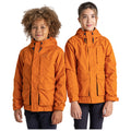 Two children stand side by side wearing bright orange jackets with hoods smiling at the camera against a plain background their hands resting at their sides while the jackets feature pockets and zippers.