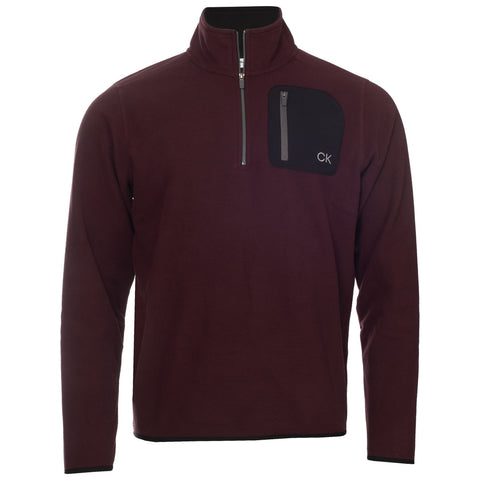 A maroon fleece pullover features a half-zip closure and a black zippered chest pocket with the initials CK displayed on it set against a neutral background