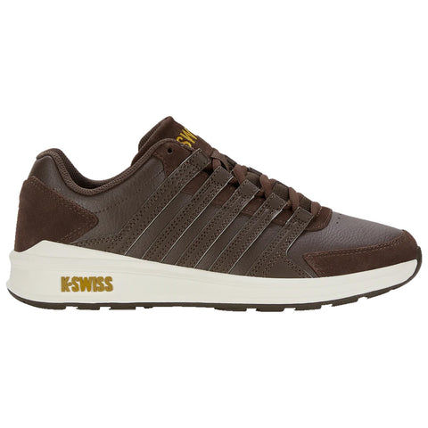 A brown athletic shoe features a textured leather upper with multiple lace loops and a white sole. The shoe is displayed against a plain background, showcasing its design and branding.