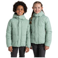 Two children stand side by side wearing light green puffy jackets with hoods smiling at the camera in a plain white background highlighting their joyful demeanor and casual attire.