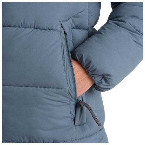 A blue puffer jacket is shown with a hand inserted into a side pocket while the other arm rests at the side. The fabric appears smooth and padded.