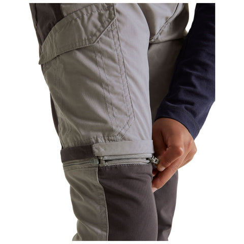 A hand is zipping up the cuff of light gray hiking pants which feature a dark gray lower section in a neutral background suggesting an outdoor or active setting.