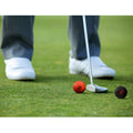 A golfer in a gray suit and white shoes prepares to putt a red ball on green grass with a putter while a black ball rests nearby.