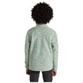 A child wearing a textured green fleece jacket with floral patterns stands with their back turned in a neutral space, hands relaxed by their sides, showcasing the colorful design on the garment.