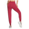 A person wears fitted, reddish jogger pants while taking a step forward in a casual setting, showcasing comfortable activewear paired with light sneakers for an athletic look.