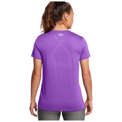 A woman stands with her back to the viewer wearing a purple athletic shirt and gray leggings in a neutral setting, showcasing the shirt's color and fit without any other prominent features.