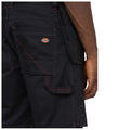 Black cargo shorts are worn by a person showing their back with visible pockets and red stitching highlighted against the fabric in an outdoor or casual environment.