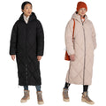 Two women stand side by side wearing long puffer coats one in black and the other in light pink both with hoods and boots in a plain background showcasing winter fashion styles