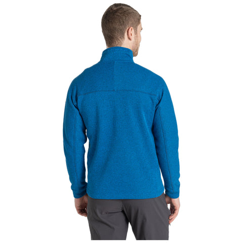 A man wearing a bright blue fleece jacket is standing with his back facing the viewer in a neutral environment, suggesting a casual or outdoor setting.