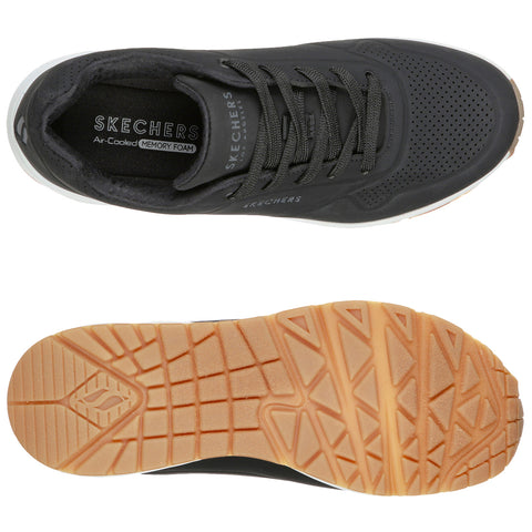 A black athletic shoe is displayed with a breathable upper and gray laces resting on a white background featuring a textured rubber outsole designed for grip and support. The insole has "SKECHERS Air-Cooled MEMORY FOAM" printed inside.