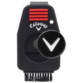 A compact black golf brush with a scrubbing bristle end and a circular button featuring a 'V' symbol is positioned upright, designed for maintaining golf clubs.