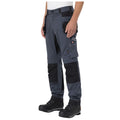 Work pants with multiple pockets are worn by a person standing. The individual is equipped for tasks, wearing sturdy black boots. The setting appears casual or work-related.