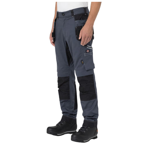 Work pants with multiple pockets are worn by a person standing. The individual is equipped for tasks, wearing sturdy black boots. The setting appears casual or work-related.