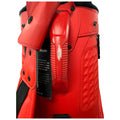 A bright red golf bag with a textured surface is positioned upright showcasing its handle and strap while a tag with text is attached to its side. The bag appears slightly worn.