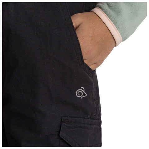 A hand is placed in the pocket of dark fabric pants featuring a small spiral logo while wearing a light green fleece sleeve that has a pink cuff.