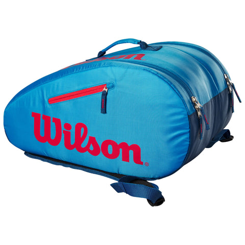 A blue and red tennis bag with multiple zippered compartments is displayed, shaped to hold gear securely, situated against a plain background, designed for easy transport and organization of sports equipment.