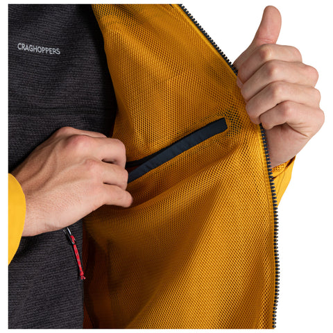 A hand pulls open a zipper on a jacket revealing a mesh interior in bright yellow. The exterior is dark gray with a logo visible on the chest area.