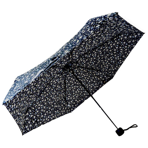 A floral-patterned umbrella is open with a dark blue background and white flowers covering its surface standing vertically against a plain white backdrop.