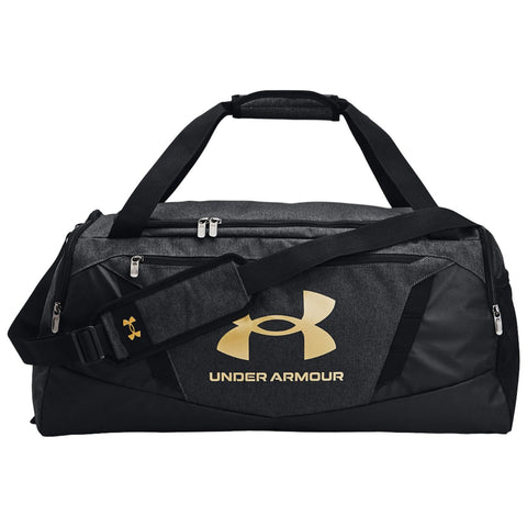 A black and gray duffel bag with the Under Armour logo prominently displayed in gold sits upright featuring dual handles and an adjustable strap for carrying.