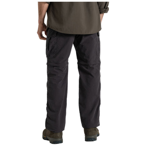 A person stands facing away wearing dark cargo pants and sturdy footwear with an olive shirt that is slightly longer at the back set against a plain white background.