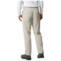 Beige cargo pants are worn by a person standing with their back to the viewer. The pants have side pockets and are paired with dark shoes. The environment is neutral and minimal.