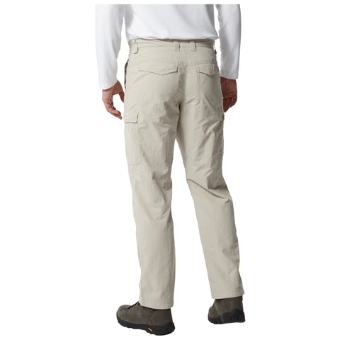 Beige cargo pants are worn by a person standing with their back to the viewer. The pants have side pockets and are paired with dark shoes. The environment is neutral and minimal.