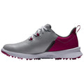 A gray and pink golf shoe is positioned sideways displaying its sleek design with a textured upper and a spiked sole intended for traction on the golf course.