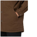 A brown outer garment features a hand resting inside a side pocket while a button closure adorns the jacket's edge suggesting casual wear in an everyday setting.