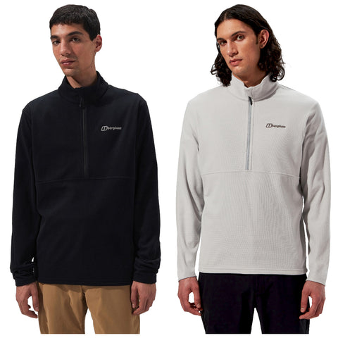 Two young men are wearing half-zip fleece pullovers in black and white styles both featuring the Berghaus logo while standing side by side in a studio setting against a plain background.