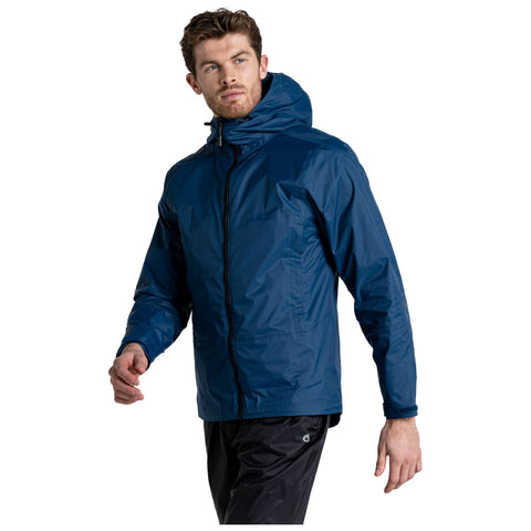 A man is walking while wearing a navy blue waterproof jacket with a hood. He has a serious expression and is in a plain white background. His pants are black.