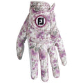 A floral-patterned golf glove rests with palm facing up showcasing shades of purple and white against a light background highlighting its intricate design and branding sewn on the wrist.