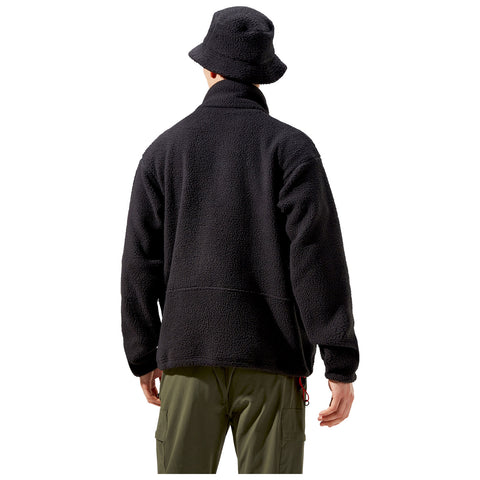 A person stands with their back facing the viewer wearing a black fleece jacket and a black bucket hat. The background is plain and minimalistic.