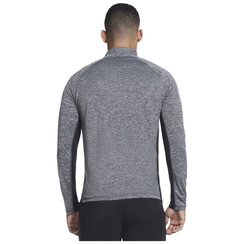 A person is wearing a gray long-sleeve athletic shirt that features dark side panels while facing away in a neutral setting likely intended for sports or physical activities.