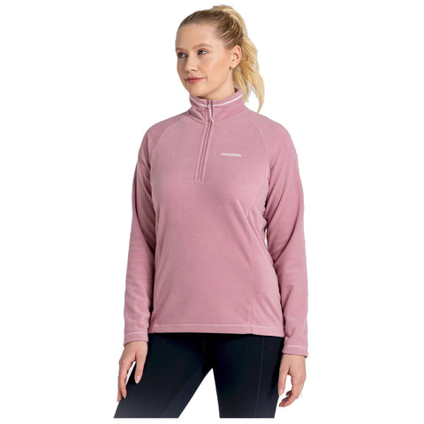 A person is wearing a light pink zip-up fleece sweater with long sleeves and a high collar standing in a neutral environment with an expression of calmness and confidence.