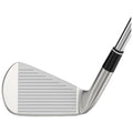 A golf club head is shown tilted slightly to one side resting on a flat surface with grooved striking surface visible and shiny metallic finish highlighting its design and angle.