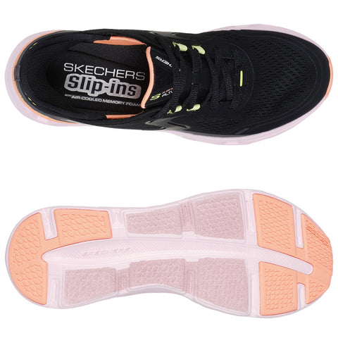 Black athletic shoe features a slip-on design with air-cooled memory foam cushioning and contrasting pink accents on the sole providing comfort for active use or casual wear. Text reads "SKECHERS SLIP-INS AIR-COOLED MEMORY FOAM."