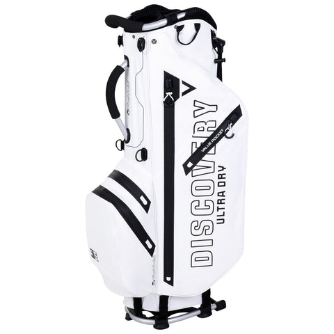 A white golf bag stands upright featuring multiple zippered pockets and a prominent logo. It is designed for carrying golf clubs and accessories, suitable for use on a golf course.