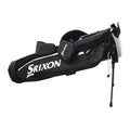 A black golf bag with the Srixon logo is standing upright with a retractable support leg extended the bag has multiple compartments and padded straps for carrying.