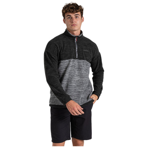 A young man wearing a black and gray half-zip pullover and black shorts stands confidently with a slight smile in a neutral background. He appears ready for casual outdoor activity.