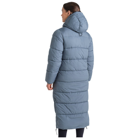 A woman is standing in a long, gray puffer coat with a hood showcasing its puffy, quilted design in a neutral space emphasizing warmth and comfort in cold weather.