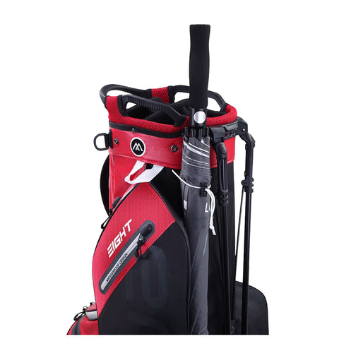 A red golf bag stands upright featuring an umbrella secured at the top showcasing a sleek design with various pockets and a logo prominently displayed on the side.