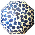 A round umbrella with a design of dark blue dots on a light background is opened and positioned upward, providing shade or protection from rain in an outdoor setting.